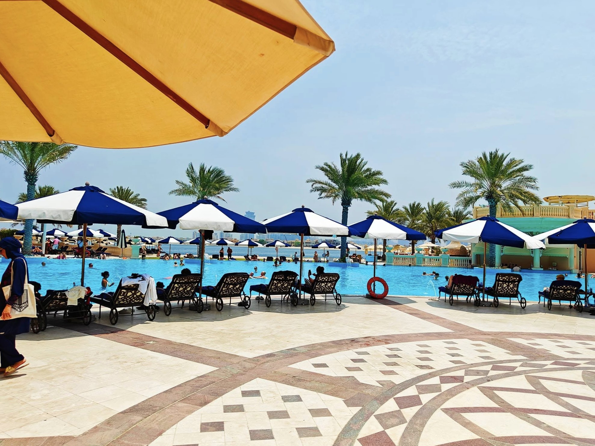 Infinity pool at Raffles The Palm Dubai overlooking the Arabian Gulf, lined with sun loungers, palm trees, and the resortβs grand palace-style architecture in the background.