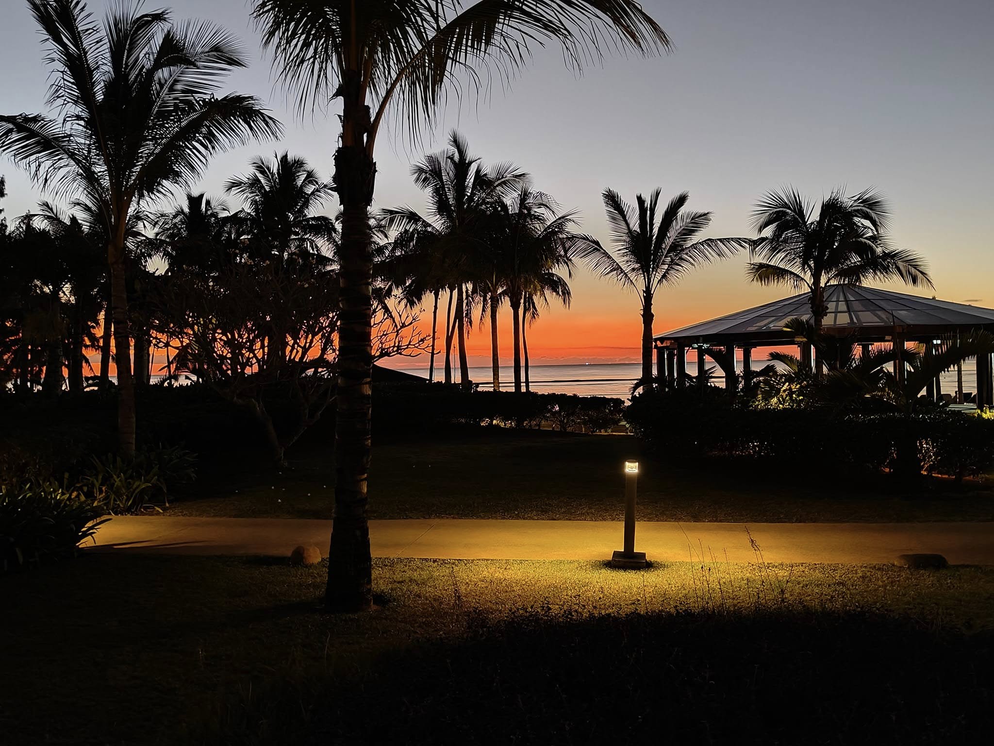 Golden hour light washing over the pool and gardens at Le Mรฉridien Mauritius, casting a warm amber glow across the resort