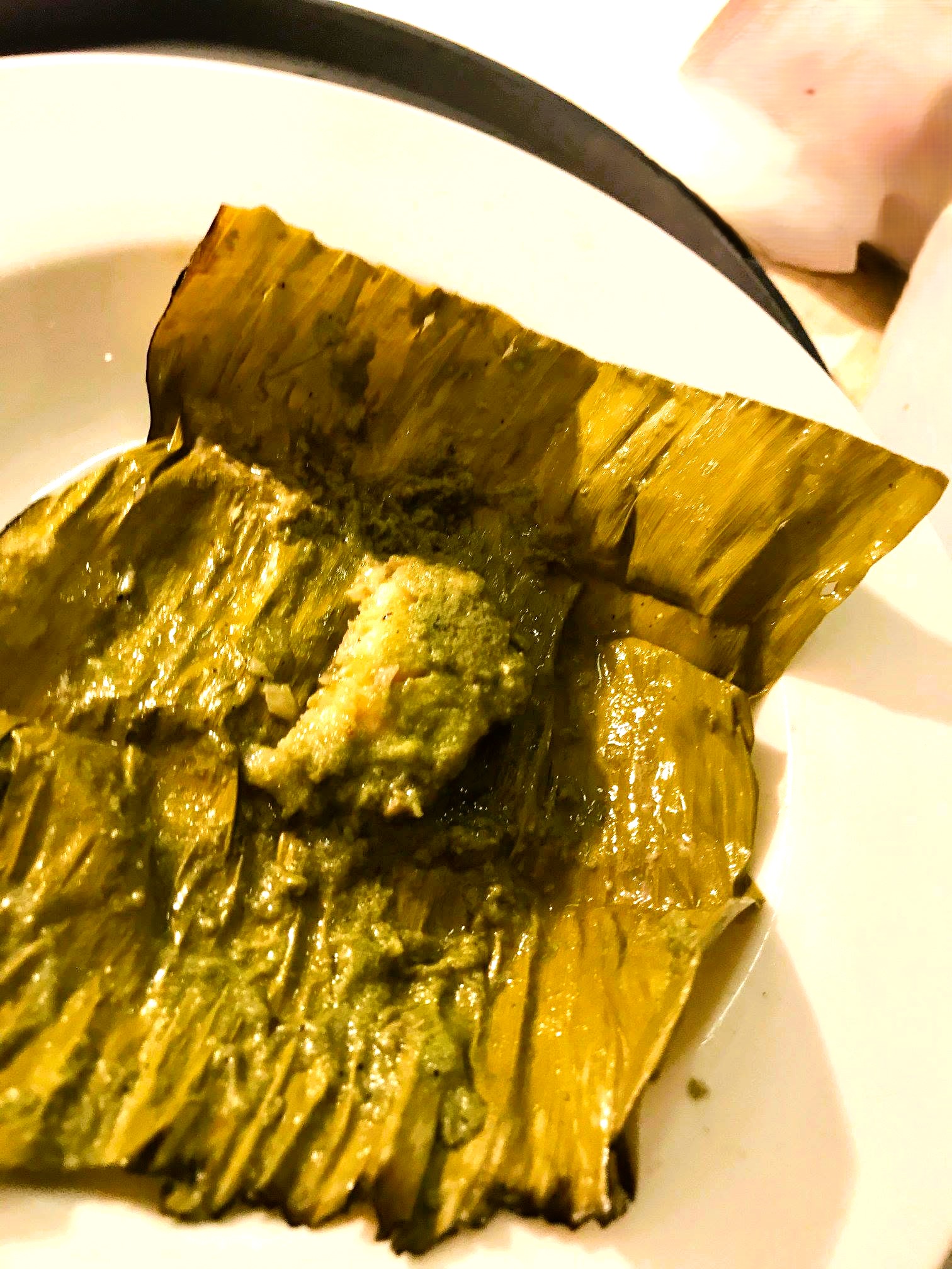Steamed Parsi Patrani Machhi wrapped in banana leaf, topped with vibrant green chutney and served on a plate.